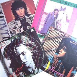 Peut inclure: Quatre pochettes de disques vinyles carrées présentant des portraits d'artistes musicaux. Une pochette montre une personne avec un cheval, une autre comporte du texte en cyrillique, et les autres affichent des photos stylisées avec des graphismes.