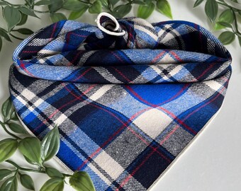 Peut inclure: Un bandana triangulaire pour animal avec un motif à carreaux dans des tons bleu marine, bleu vif, crème et de fines lignes rouges. Le tissu présente un bord supérieur replié avec une petite boucle élastique blanche pour le fixer.