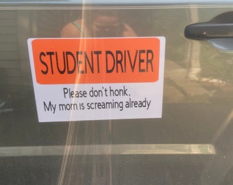 May include: An orange and white sign on a gray car that reads "STUDENT DRIVER" and "Please don't honk, My mom is screaming already."