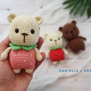 May include: Three crocheted teddy bears, one in pink with a strawberry design, one in white with a red strawberry design, and one in brown.  The bears are all handmade and have black eyes and a brown nose.