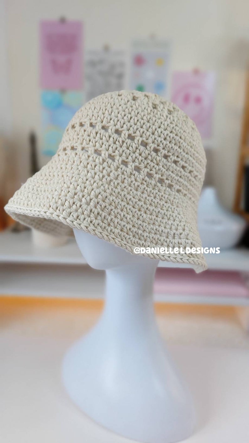 May include: A crocheted sun hat in a cream color with a wide brim and an open weave pattern. The hat is displayed on a white mannequin.