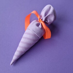 May include: A purple fabric cone-shaped pouch with a striped pattern tied with an orange ribbon.
