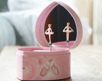 May include: A pink heart-shaped music box with a ballerina figurine inside. The box has a white and pink floral design and a mirror on the lid.