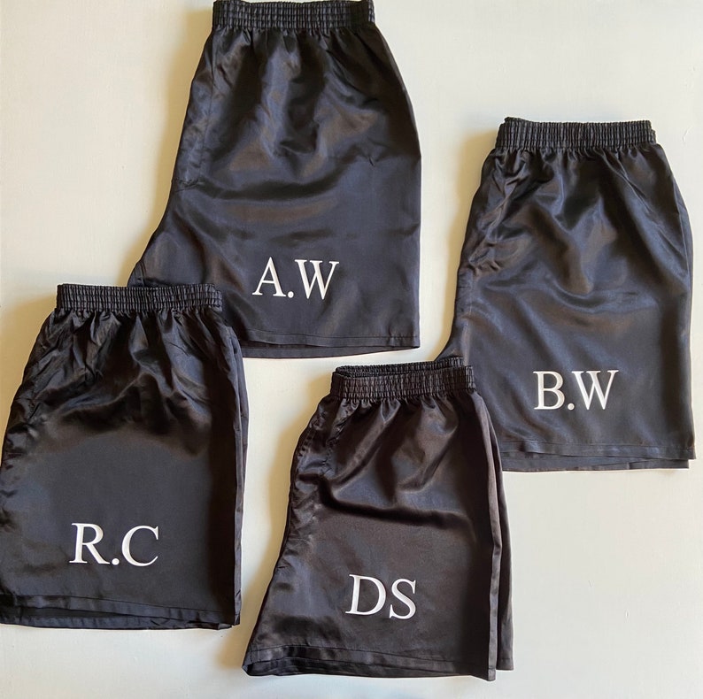 Pode incluir: Quatro pares de cal&ccedil;&otilde;es de cetim preto com iniciais bordadas a branco. As iniciais s&atilde;o "A.W.", "B.W.", "R.C." e "D.S."