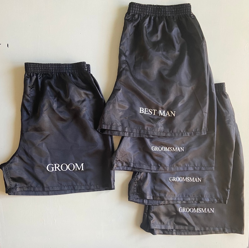 Pode incluir: Cinco cal&ccedil;&otilde;es de desporto de nylon preto com texto branco. Os cal&ccedil;&otilde;es est&atilde;o empilhados uns sobre os outros. O cal&ccedil;&atilde;o de cima diz "Best Man". Os tr&ecirc;s seguintes dizem "Groomsman". O cal&ccedil;&atilde;o de baixo diz "Groom".