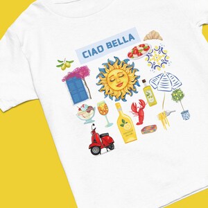 May include: White t-shirt with a colorful illustration of Italian icons, including a sun, a scooter, a glass of wine, a bottle of limoncello, a lobster, a plate of pasta, a croissant, a plate of caprese salad, a blue door, a potted olive tree, and a beach umbrella. The text "Ciao Bella" is printed in blue on a light blue background.