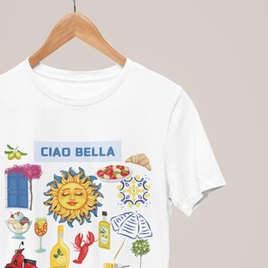 May include: White t-shirt with the text "Ciao Bella" and a colorful illustration of Italian icons, including a sun, a scooter, a lemon, a lobster, a glass of wine, a plate of pasta, a croissant, a potted lemon tree, and a blue and white striped umbrella.