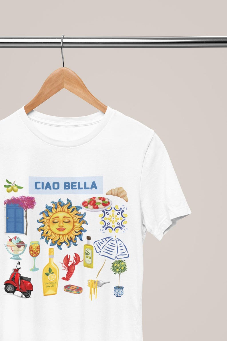 May include: White t-shirt with the text "Ciao Bella" and a colorful illustration of Italian icons, including a sun, a scooter, a lemon, a lobster, a glass of wine, a plate of pasta, a croissant, a potted lemon tree, and a blue and white striped umbrella.