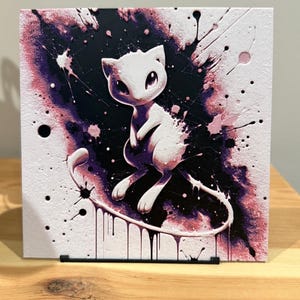 Puede incluir: Impresión artística cuadrada que presenta una criatura blanca con forma de gato y ojos grandes, sobre un fondo de salpicaduras de pintura morada y negra. La obra de arte tiene un efecto de acuarela, con goteos y salpicaduras que se suman al diseño abstracto.