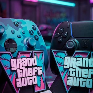Op de afbeelding: Twee videogamecontrollers, één in blauwe camouflage en één in zwart, elk gepresenteerd met een Grand Theft Auto V logo-standaard. De standaards tonen een gestileerde V met palmbomsilhouetten in taling en roze, passend bij de neonstijl van de controllers.