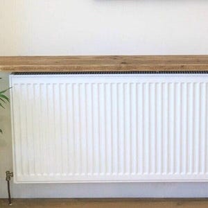 Vue de face grande tablette radiateur bois sur mesure installée sur large radiateur panneau blanc, habillage élégant et discret.