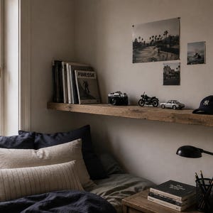 May include: A bedroom scene with a wooden shelf displaying a camera, motorcycle, car, and a baseball cap. The shelf also holds books and a magazine with the word "FINESSE". Below, a bed is made with dark blue and beige pillows and bedding.