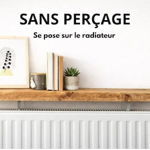 May include: A natural wood shelf mounted above a white radiator. The text SANS PER&Ccedil;AGE Se pose sur le radiateur is visible above the shelf. On the shelf are a framed print, a grey container, three books, and a small green succulent plant.