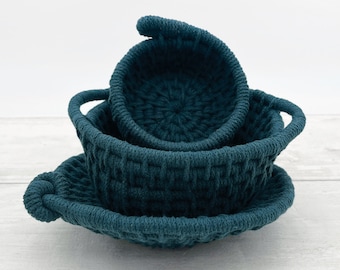May include: Three teal blue woven rope baskets of different sizes stacked on top of each other. The baskets are made of thick rope and have a woven pattern.