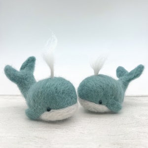 May include: Two small, teal blue felt whale figurines with white felt accents. The whales have white felt spouts and black felt eyes.