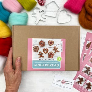 Puede incluir: Un kit de fieltro con aguja para crear adornos navideños con temática de pan de jengibre. La caja, etiquetada como "Needle-Felting Kit Gingerbread", contiene lana de varios colores, cortadores de galletas e instrucciones.