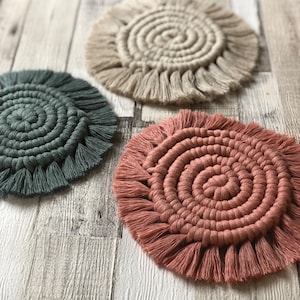 Puede incluir: Tres posavasos redondos de crochet con flecos. Los posavasos son en tonos de verde, beige y rosa.