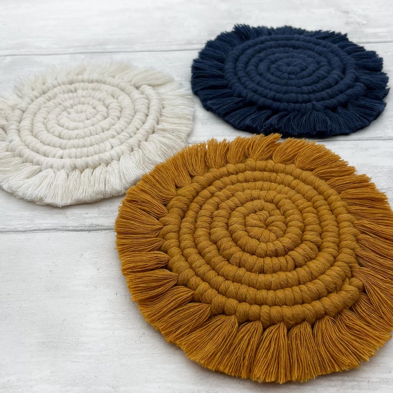Puede incluir: Tres posavasos redondos de crochet con flecos. Los posavasos son de color blanco, amarillo mostaza y azul marino.