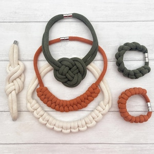 May include: Set of four knotted rope necklaces and bracelets in green, orange, and white. The necklaces are layered and feature a variety of knot patterns. The bracelets are simple and elegant.