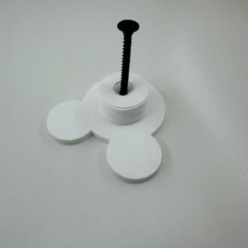 以下が含まれることがあります： ミッキーマウスの頭の形をした白い3Dプリントオブジェクト。白いディスクのスタックと黒いネジが付いています。このオブジェクトはネジを固定するように設計されています。白い表面に置かれています。