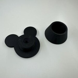 以下が含まれることがあります： 黒色の3Dプリントボトルストッパーセット。片方はミッキーマウスの頭の形で、2つの円形の耳と中央の円盤があります。もう片方は、内部にネジ山が切られた円錐形のスリーブです。