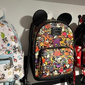 以下が含まれることがあります： 黒いミッキーマウスの耳が付いた、ハロウィーンをテーマにしたカラフルなミニバックパック。バックパックには、幽霊、カボチャ、コウモリなど、さまざまな不気味なキャラクターやオブジェクトが描かれています。フロントポケットとLoungeflyのロゴが付いています。