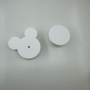 以下が含まれることがあります： 2つの白いキャビネットノブ。1つはミッキーマウスの頭の形をしており、耳の2つの小さな円と頭の大きな円があります。もう1つのノブは、シンプルな円です。