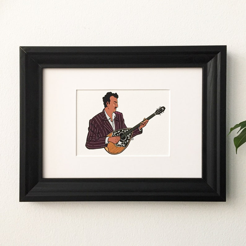 May include: A framed illustration of a person playing a bouzouki, a traditional Greek musical instrument. The person is wearing a striped suit and has dark hair. The bouzouki is brown with white accents.