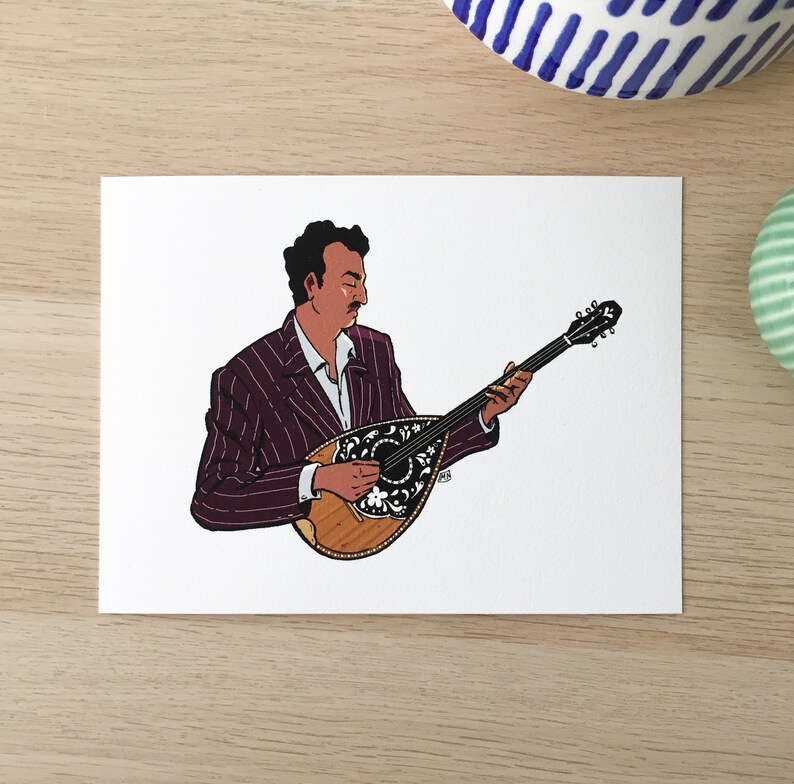 May include: A man in a purple striped suit plays a bouzouki, a traditional Greek stringed instrument. The bouzouki has a wooden body and a decorative floral design.