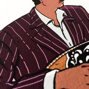 May include: A close-up of a man wearing a pinstripe suit jacket with a white shirt underneath. The jacket is a dark burgundy color with thin pink stripes. The man is holding a musical instrument in his hands.