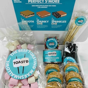 May include: A white box filled with ingredients for making s'mores. The box includes a can of marshmallows, a bag of chocolate chips, a bag of graham crackers, and a bag of sprinkles. The box also includes a small wooden stick for roasting marshmallows.
