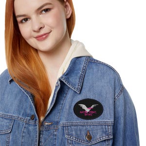 May include: A blue denim jacket with a black oval patch. The patch displays a white bat with pink details and the pink text "MAYBE TODAY, SATAN". The jacket is a medium wash.