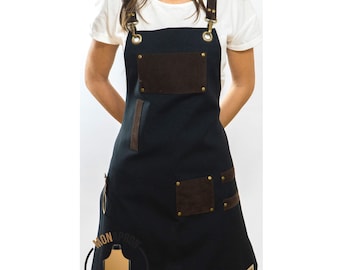 May include: Black canvas apron with brown leather accents and adjustable straps. The apron has two large pockets and a smaller pocket on the front. The apron is branded with the text "Mon Apron".