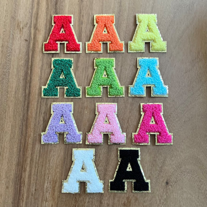 May include: Ten felt letter patches in various colors, each featuring the letter 'A'. The patches are arranged in two rows of five, with the colors alternating from red to orange, yellow, green, blue, purple, pink, white, and black.