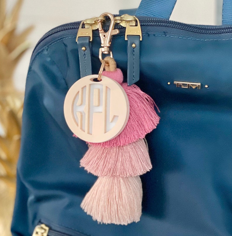 May include: A pink and white tassel keychain with a round wooden charm featuring the monogram "KPL".