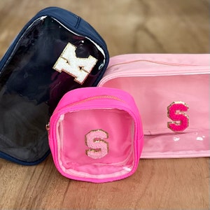 May include: Three clear cosmetic bags with pink and navy blue fabric exteriors. The bags have gold zippers and feature a large letter appliqu&eacute; on the front. The letters are K, S, and S.