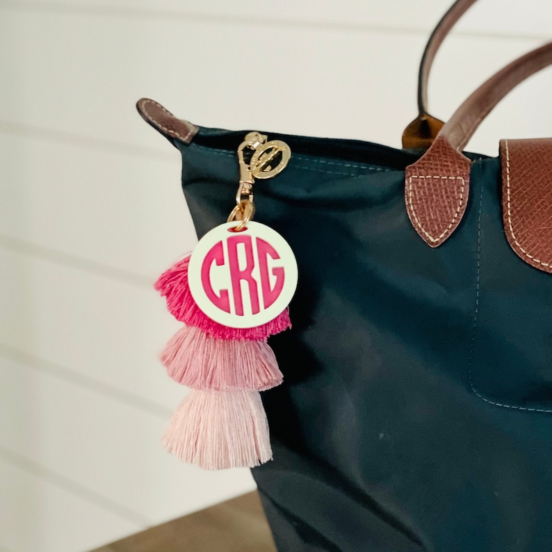 May include: A pink and white tassel keychain with a white circle charm featuring the monogram "CRG" in pink letters.
