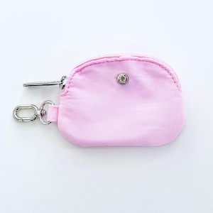 Puede incluir: Una peque&ntilde;a bolsa rosa con cremallera, un anillo plateado y un cierre de presi&oacute;n plateado.