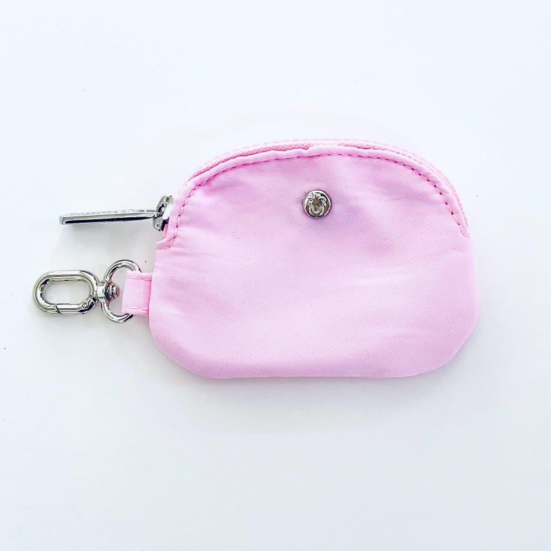 Puede incluir: Una peque&ntilde;a bolsa rosa con cremallera, un anillo plateado y un cierre de presi&oacute;n plateado.