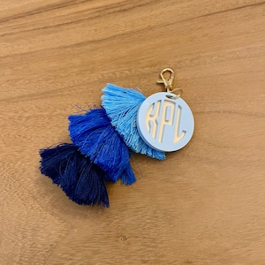 May include: A blue and navy tassel keychain with a light blue circle charm with the initials "KPL" in white.