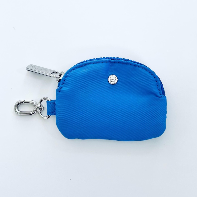 Puede incluir: Una peque&ntilde;a cartera de monedas de color azul brillante con una cremallera plateada y un cierre de bot&oacute;n plateado. La cartera tiene un llavero.