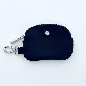 Puede incluir: Una peque&ntilde;a cartera de monedas negra con cremallera, con un tirador de cremallera de metal plateado y un bot&oacute;n de metal plateado. La cartera es peque&ntilde;a y compacta, ideal para llevar monedas o art&iacute;culos peque&ntilde;os.