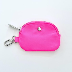 Puede incluir: Una peque&ntilde;a bolsa rosa brillante con cremallera y un tirador de cremallera plateado y un cierre de bot&oacute;n plateado. La bolsa tiene un llavero.