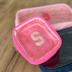 May include: A pink clear makeup bag with a pink fluffy letter "S" on the front. The bag has a zipper closure and a clear plastic window.
