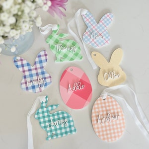 May include: Seven Easter-themed gift tags with gingham patterns in various colors. Each tag features a bunny or egg shape with a name written in white script: Nora, Thomas, Emily, Addie, James, Chloe, and Andrew.