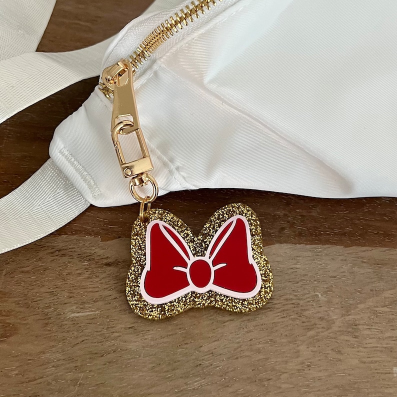 May include: A white bag with a gold zipper and a gold chain attached to a red glitter bow charm.