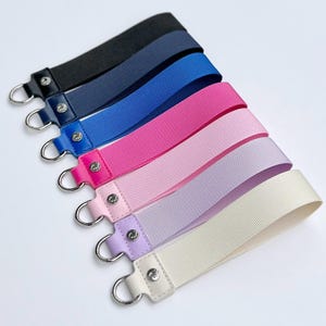 May include: Seven different colored ribbon keychains with silver rings. The colors are black, navy blue, royal blue, pink, light pink, lavender, and cream.