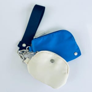 May include: Two small zippered pouches with a black strap and silver hardware. The top pouch is blue and the bottom pouch is cream.