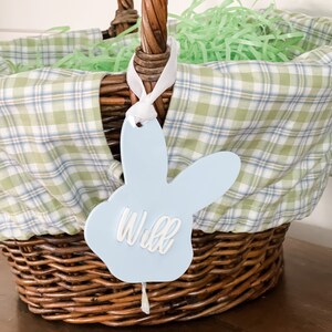 May include: A blue bunny-shaped Easter basket tag with the name "Will" written in white lettering.