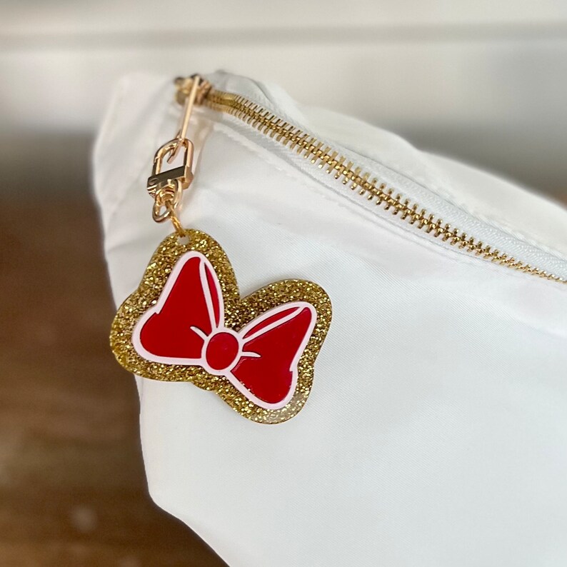 May include: A white bag with a gold zipper and a gold glitter bow charm with a red center.